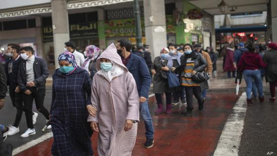 People wearing face masks to protect against the spread of coronavirus, cross a busy street during rainfall, in Rabat, Morocco, Monday, Dec. 14, 2020. (AP Photo/Mosa'ab Elshamy)