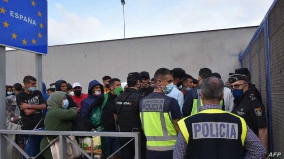 Spanish policemen stand next to migrants waiting to cross the border back to Morocco at the Spanish enclave of Ceuta on May 20, 2021. - Spain accused Morocco of "blackmail" on for allowing a record 8,000 migrants to reach the Spanish North African enclave of Ceuta, sparking a crisis that saw clashes on the Moroccan side of the border overnight. (Photo by Antonio Sempere / AFP)